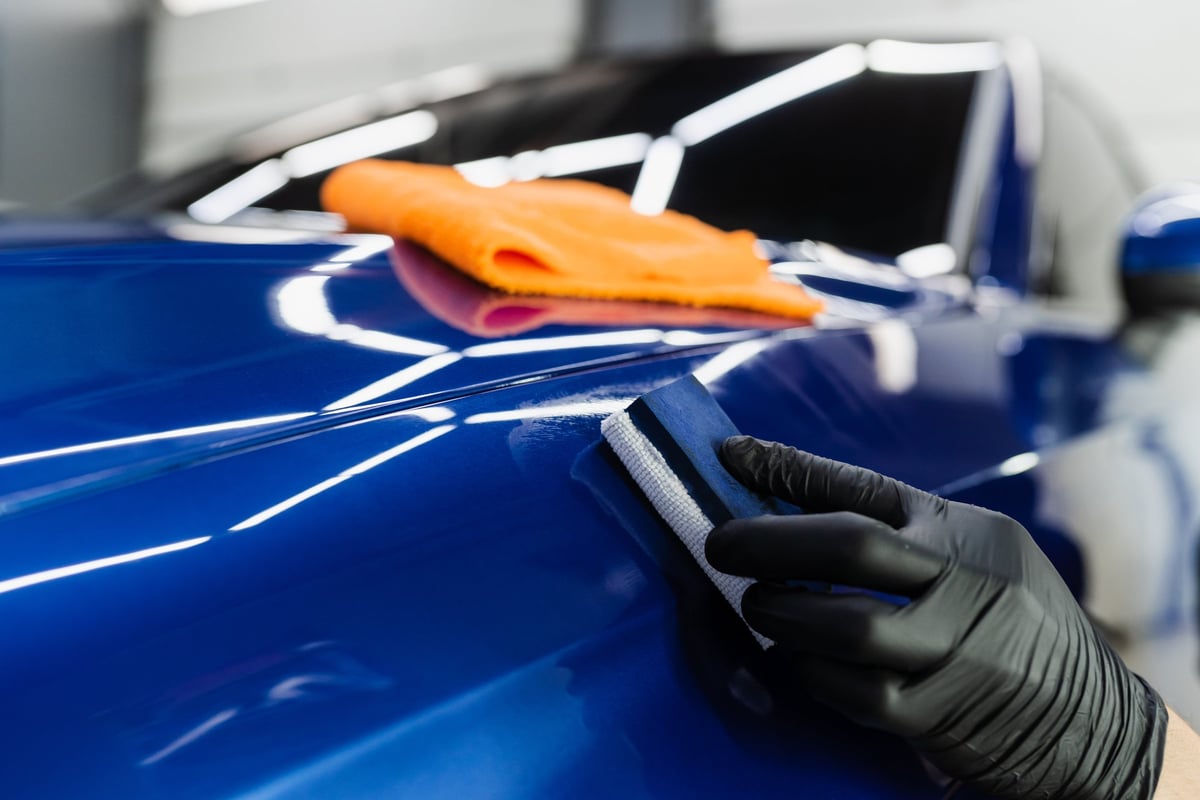 Detailer applying a protective ceramic coat to a car body with an applicator sponge