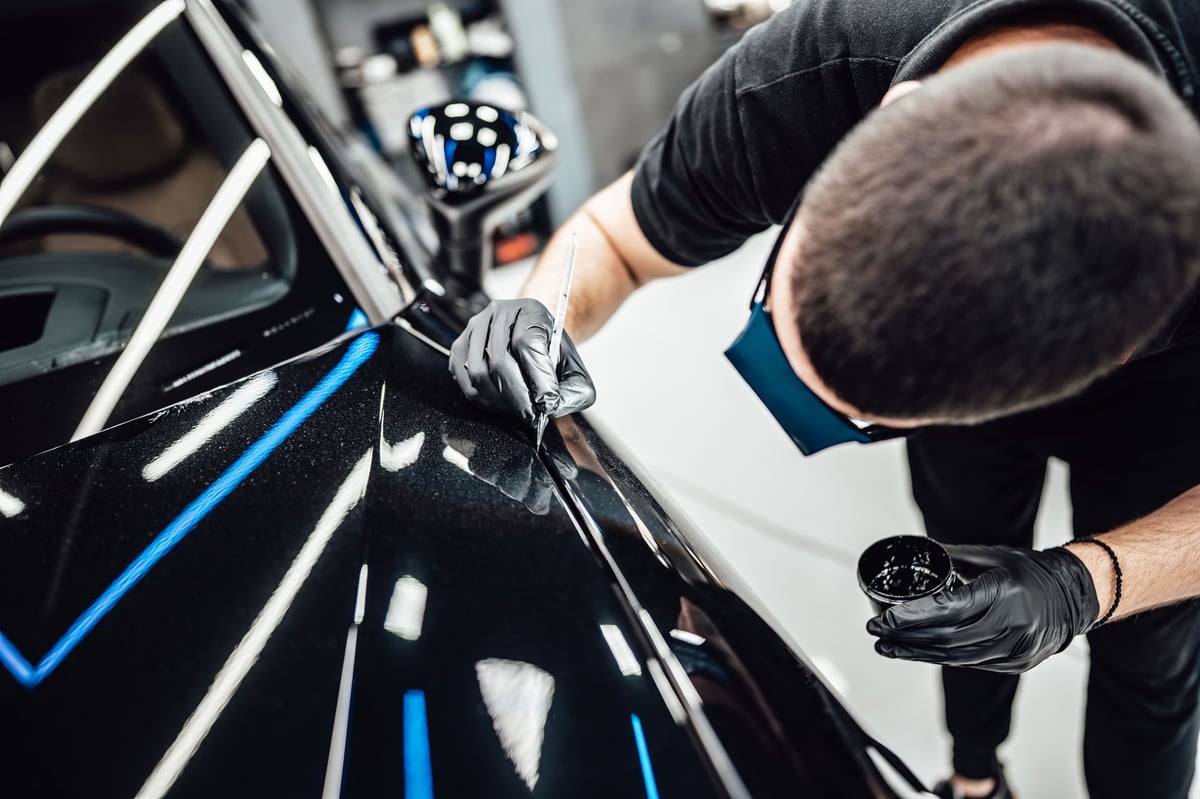 Technician machine-polishing scratches out of a luxury car's paint at a detailing centre