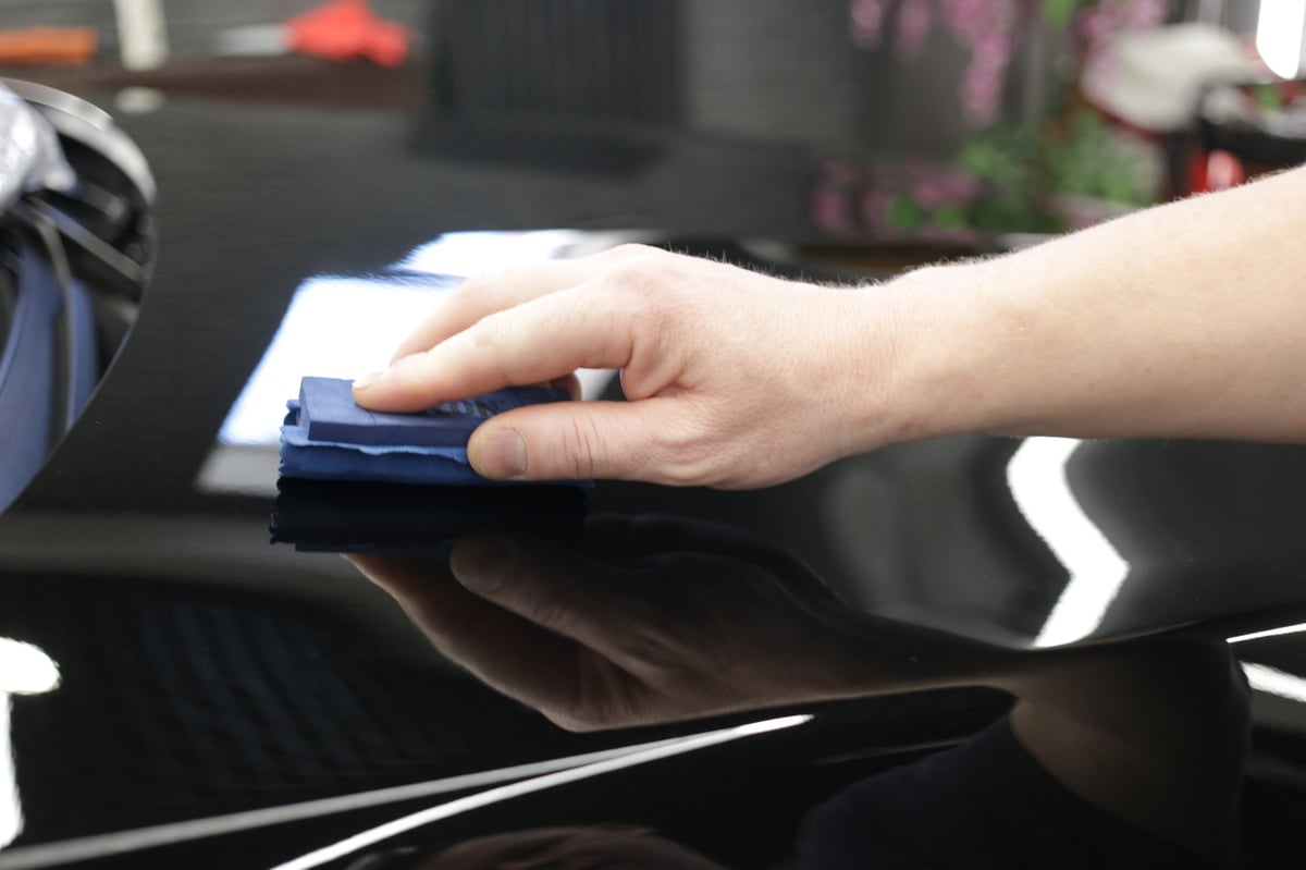 Close-up of a hand applying nano ceramic coating to a black car bonnet