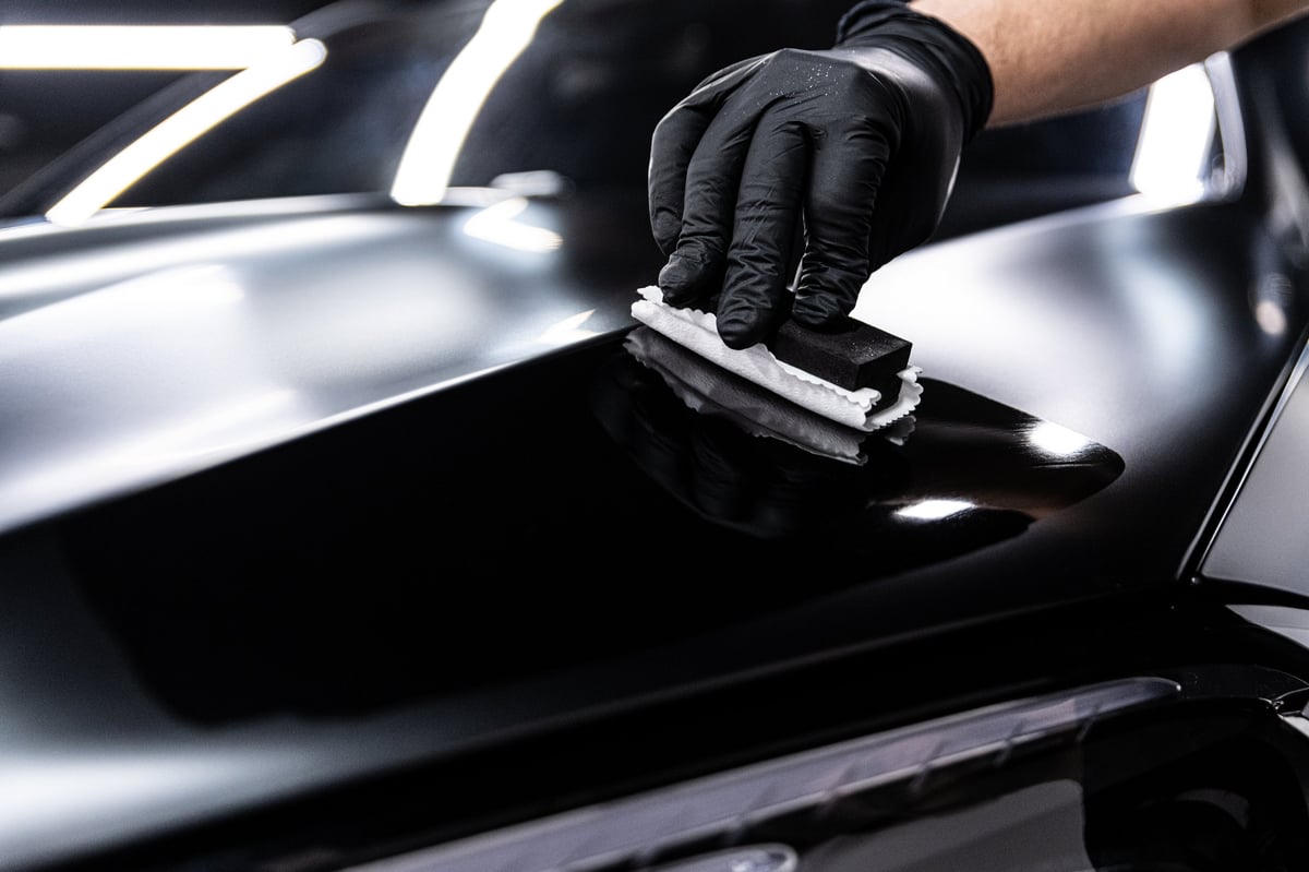 Detailer applying a ceramic coating to the deep gloss black paint of a luxury car under studio lighting