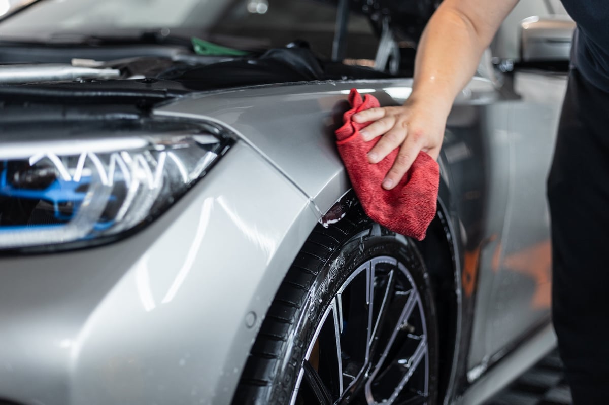Detailer wiping down and drying a car's paintwork with a microfiber cloth